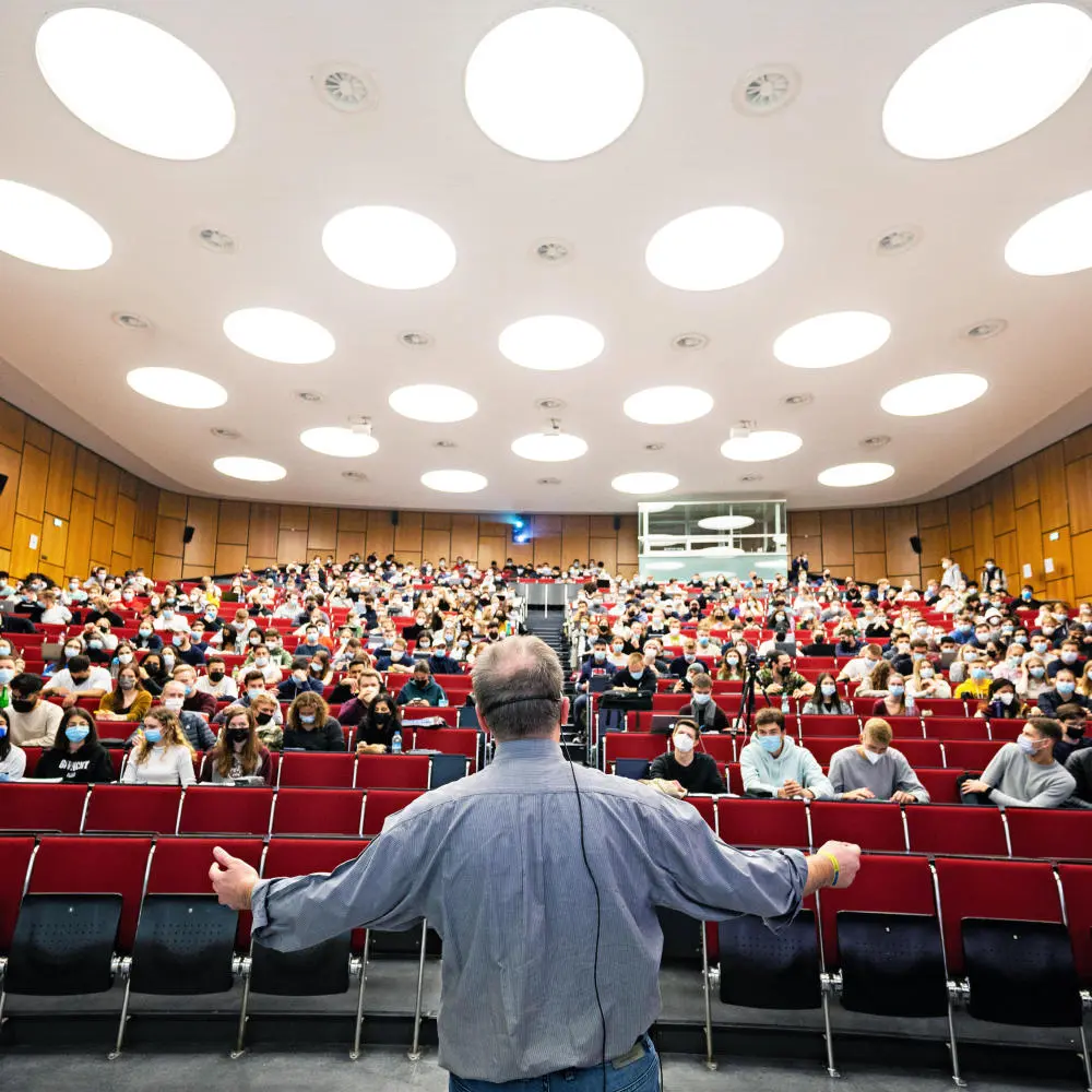 Ein Professor steht mit dem Rücken zur Kamera in einem vollen Hörsaal.