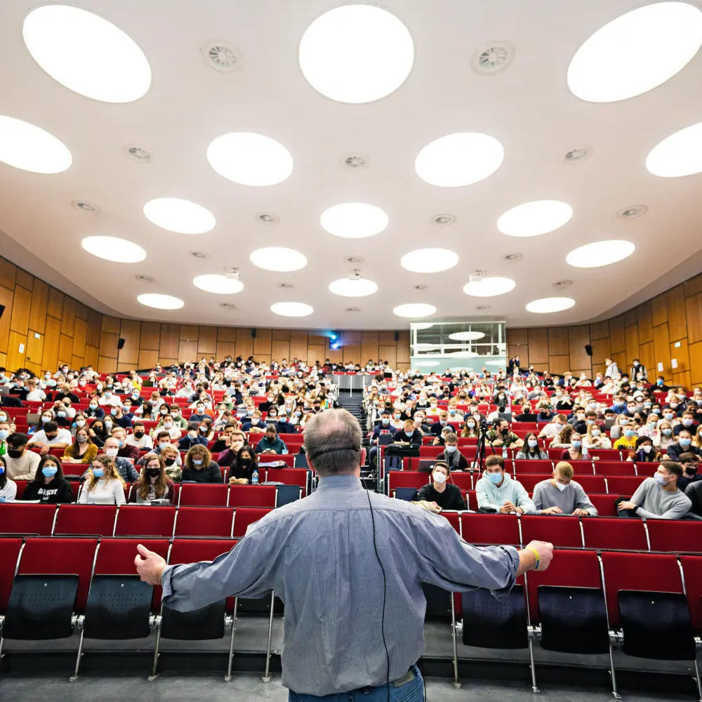 Voller Hörsaal, leere Geldbörsen: Im Jahr 2020 erhielten nur elf Prozent der Studierenden BAföG. Ein Professor steht mit dem Rücken zur Kamera in einem vollen Hörsaal.