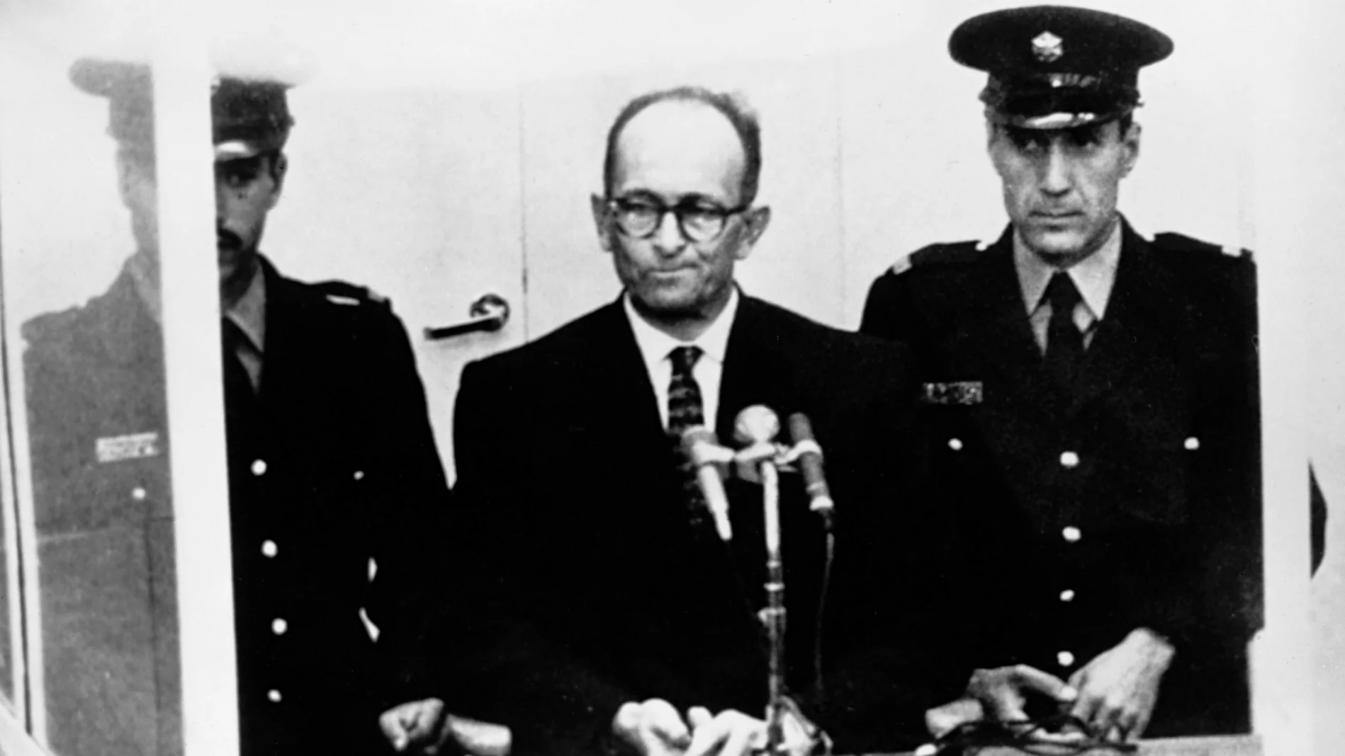 Adolf Eichmann bei seinem Prozess neben zwei Polizisten