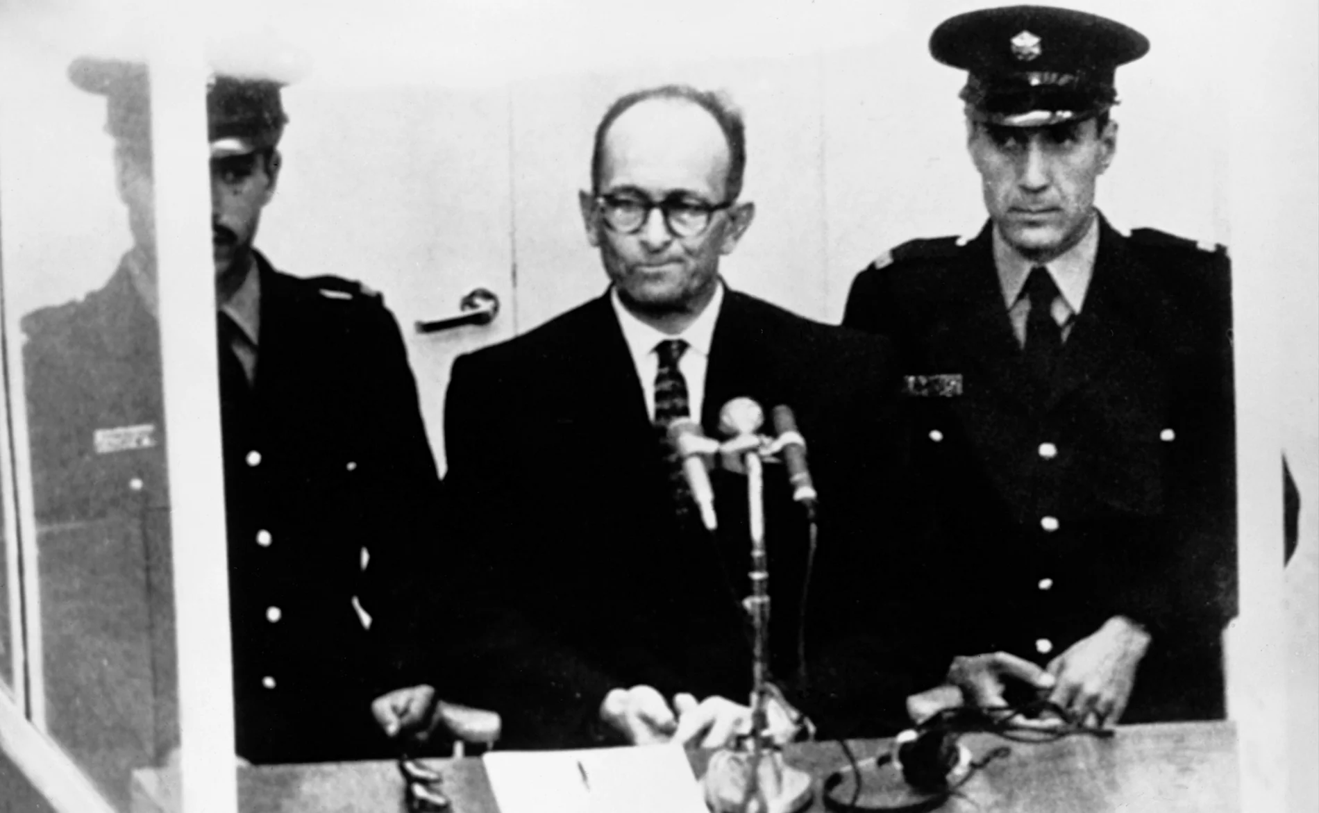 Adolf Eichmann bei seinem Prozess neben zwei Polizisten