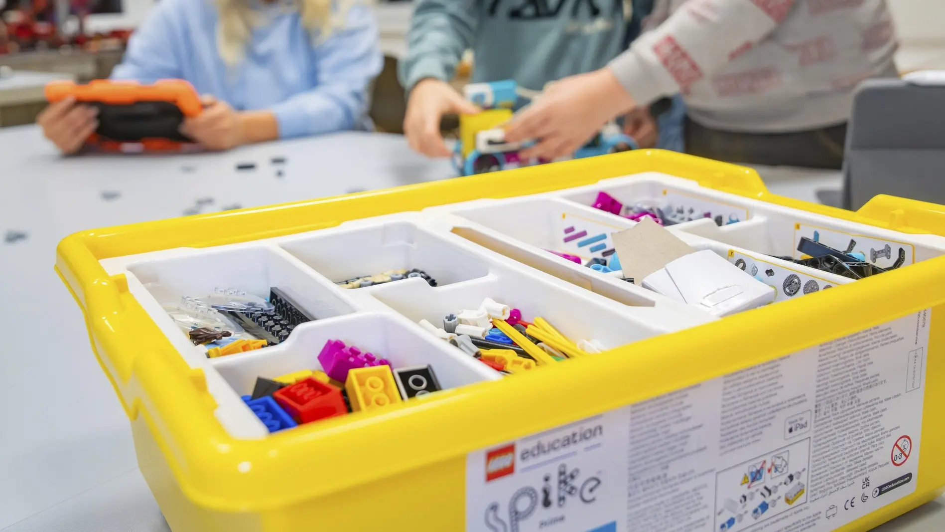 Kinder spielen mit einem gelben Lego-Set auf einem Tisch.