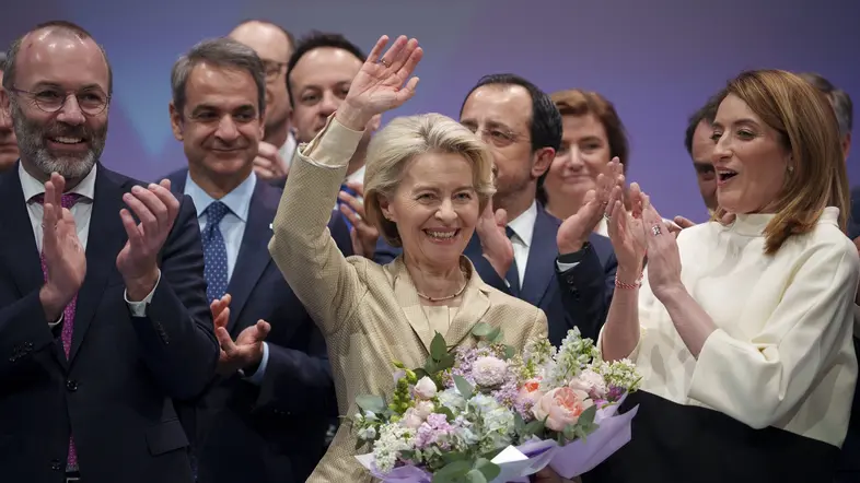 Ursula von der Leyen winkend mit einem Blumenstrauß, von Menschen umgeben