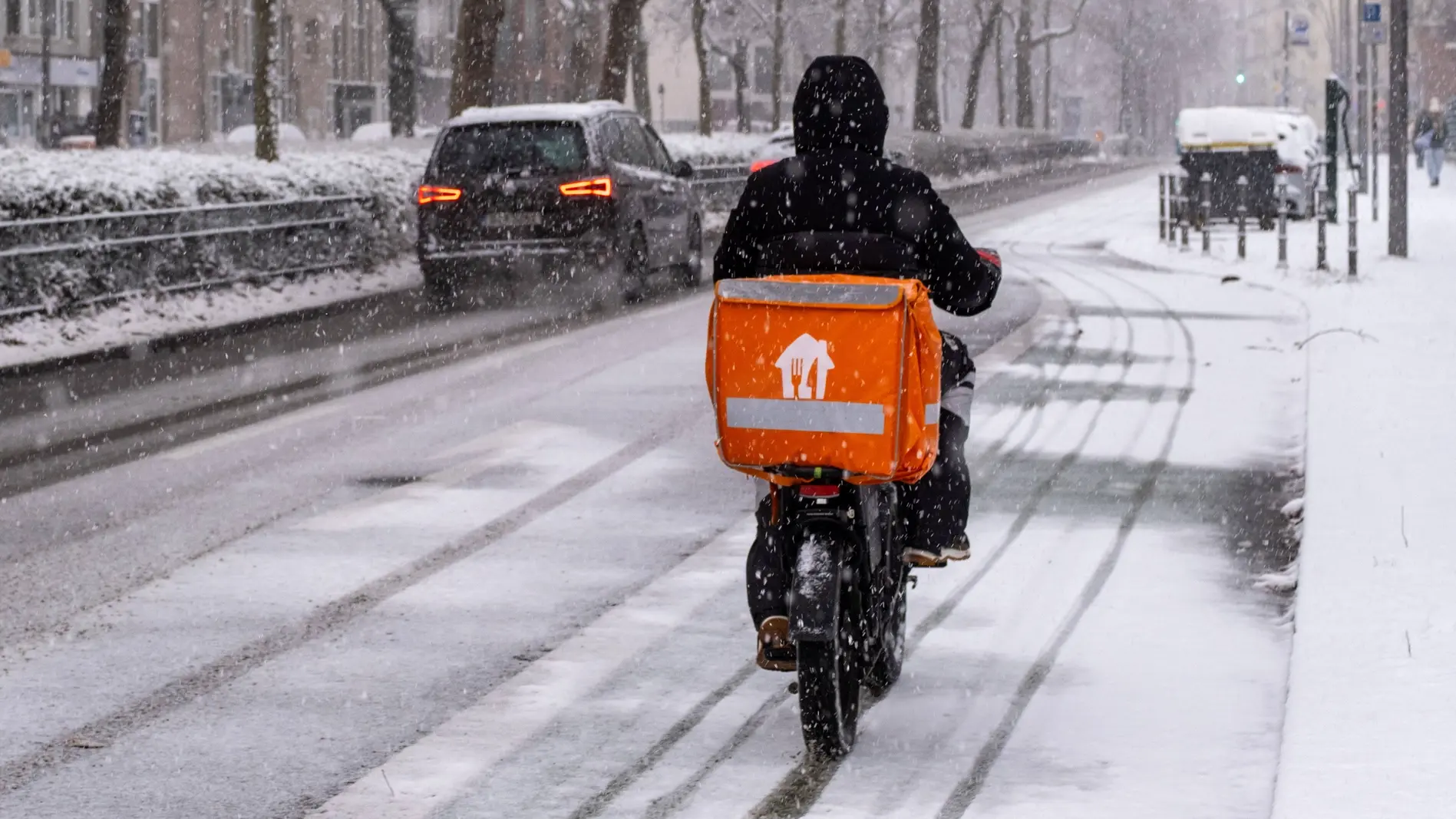 Lieferando-Fahrer mit seinem Fahrrad auf einer schneebedeckten Straße in Berlin.