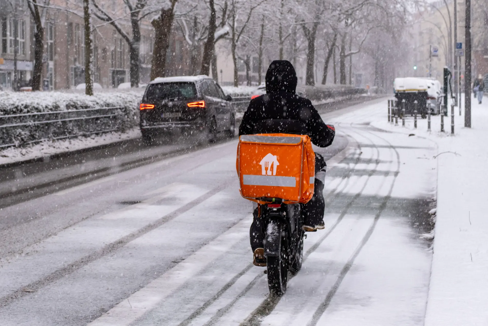 Lieferando-Fahrer mit seinem Fahrrad auf einer schneebedeckten Straße in Berlin.