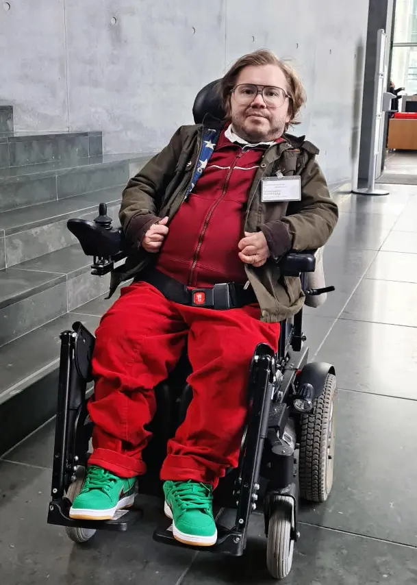 Maximilian Schulz im roten Outfit, sitzend in seinem Rollstuhl