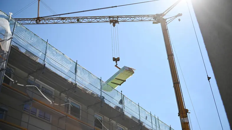 Am Kran hängen Baumaterialen für ein hohes Wohnhaus