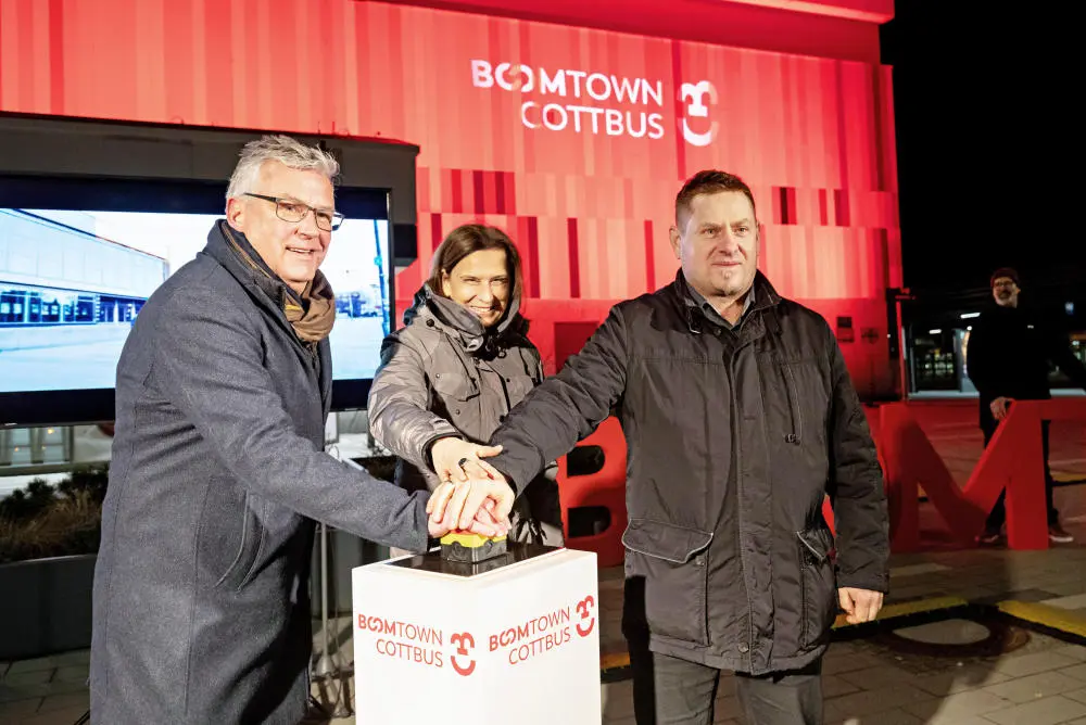 Start der "Boomtown Cottobus"-Kampagne Zwei Männer und eine Frau in Winterkleidung drücken auf einen Buzzer.