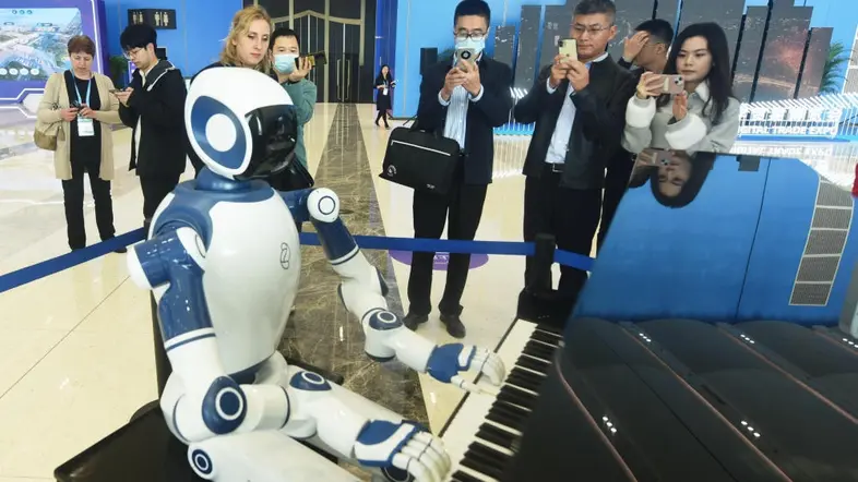 Ein Roboter sitzt an einem Klavier, beobachtet von Besuchern auf einer Messe