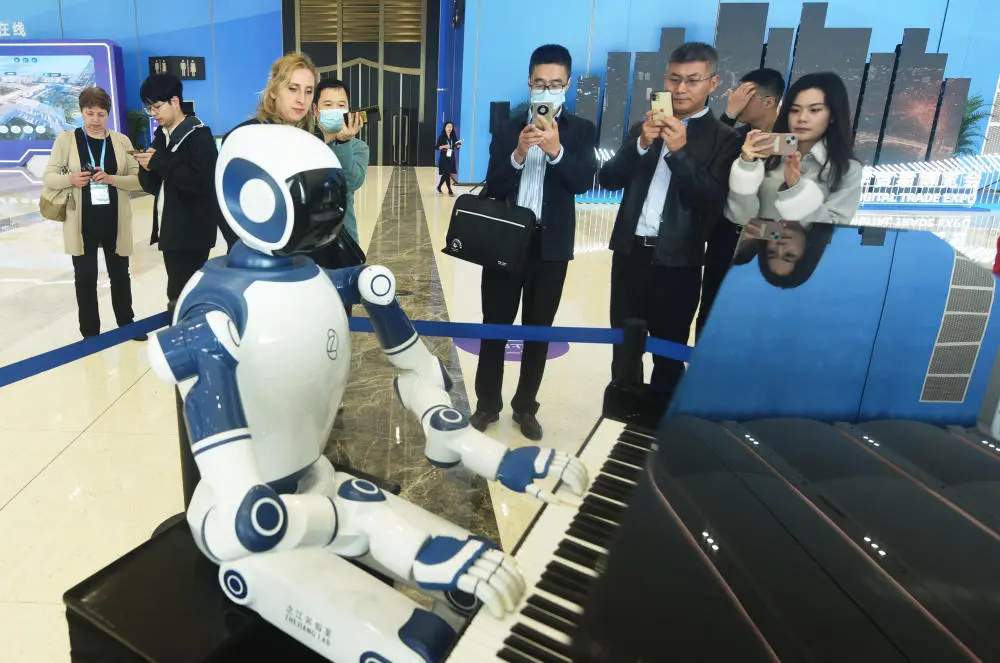 Ein Roboter sitzt an einem Klavier, beobachtet von Besuchern auf einer Messe