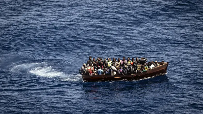 Ein kleines Boot auf dem Wasser überfüllt mit vielen Menschen, von oben fotografiert.