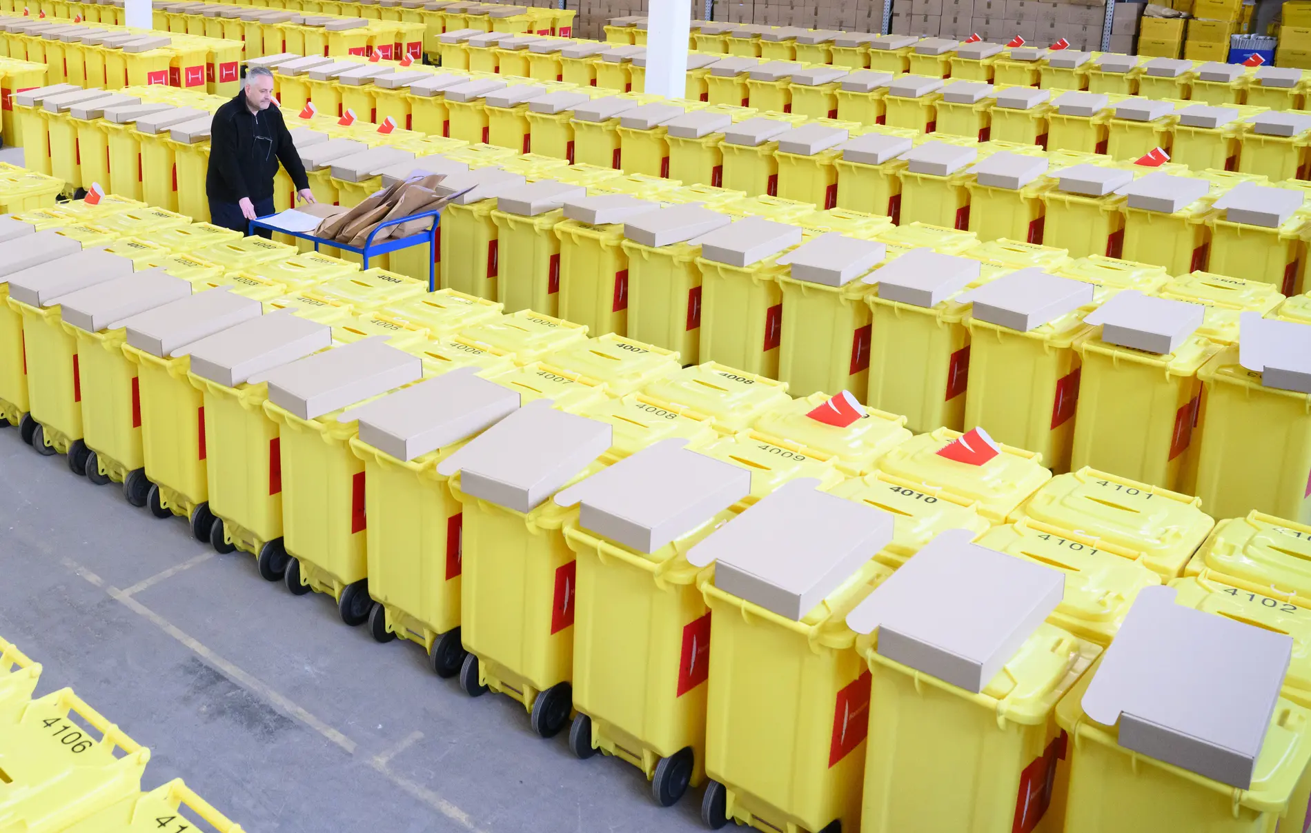 Briefwahl 2025 Mann läuft zwischen reihweisen gelben Wahlurnen mit einem Wagen herum