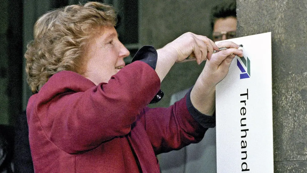Birgit Breul im roten Blazer schraubt das Schild der Berliner Treuhand-Zentrale ab.