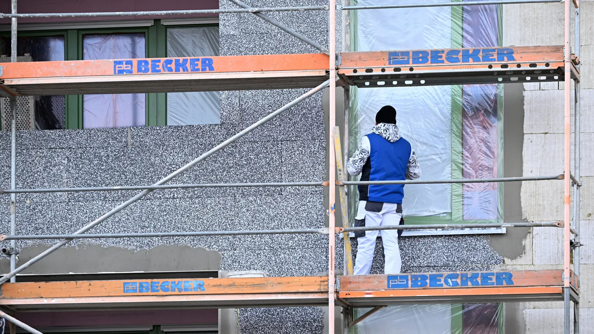 Fassadendämmung am Neubau Auf eine Fassade eines Neubauhauses wird eine Dämmschicht aufgesetzt.