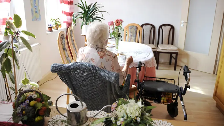 Eine ältere Frau sitzt alleine an einem Tisch