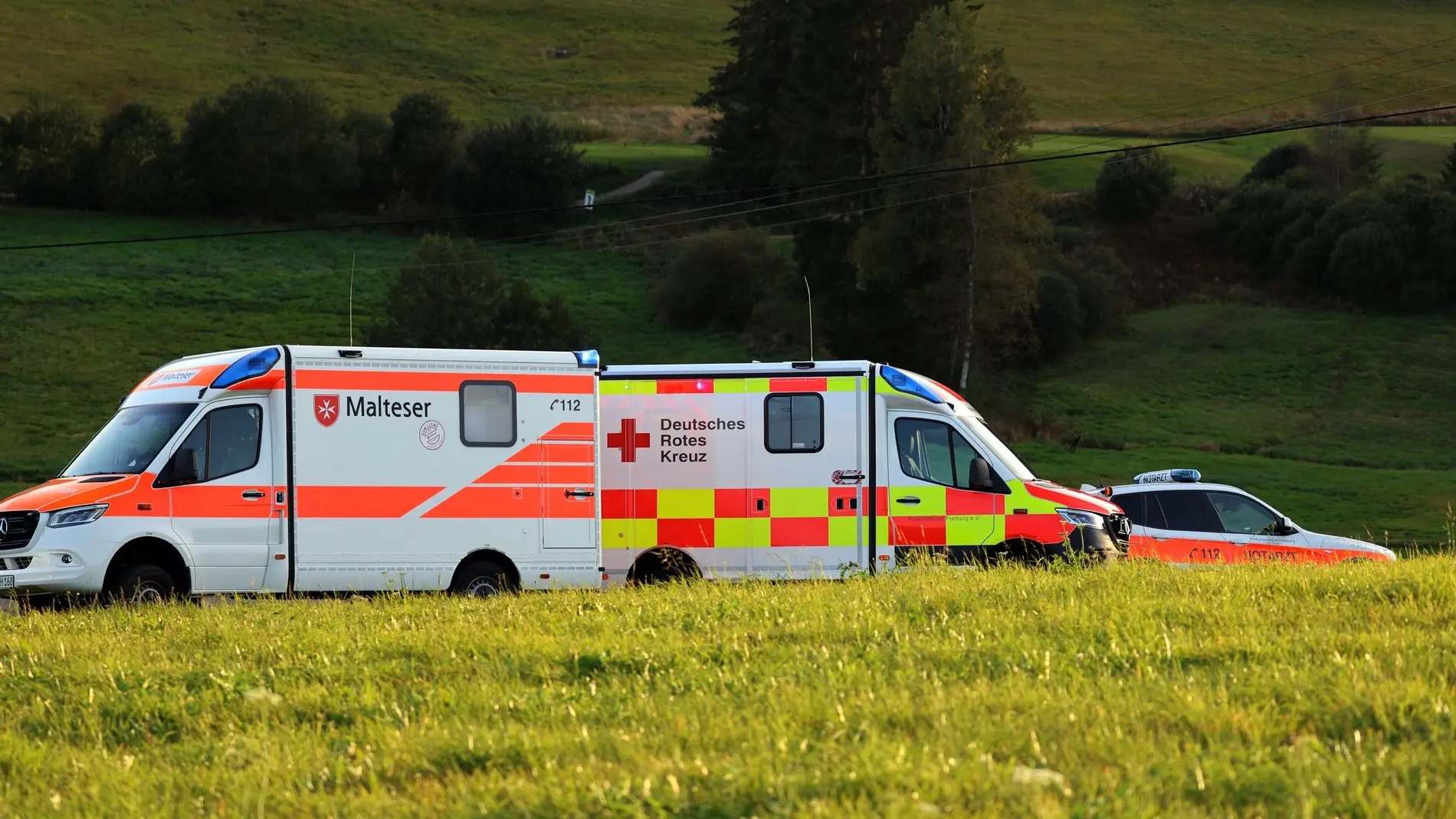 Rettungsfahrzeuge von DRK und Malteser stehen an einem Feldrand.