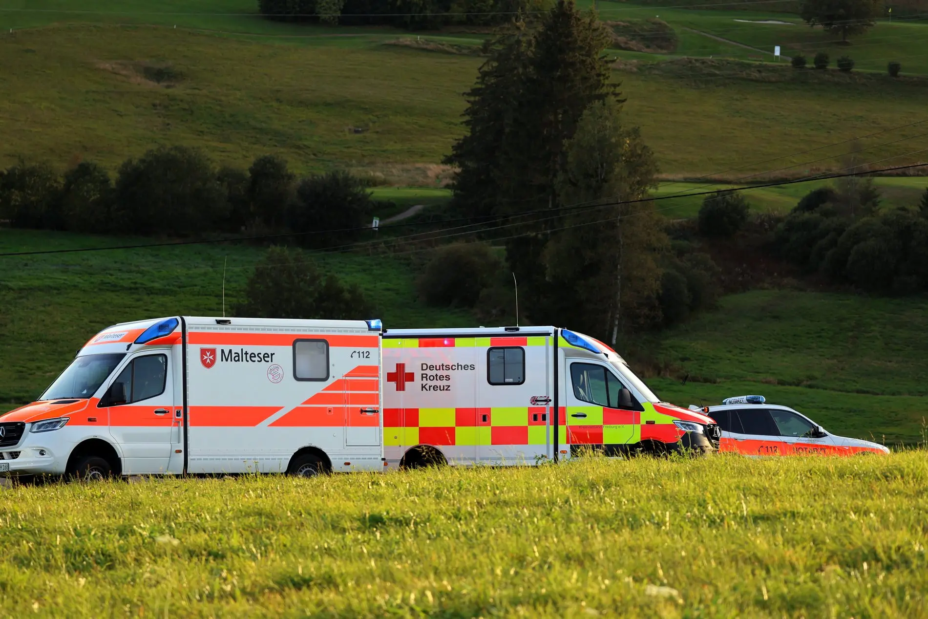 Rettungsfahrzeuge von DRK und Malteser stehen an einem Feldrand.