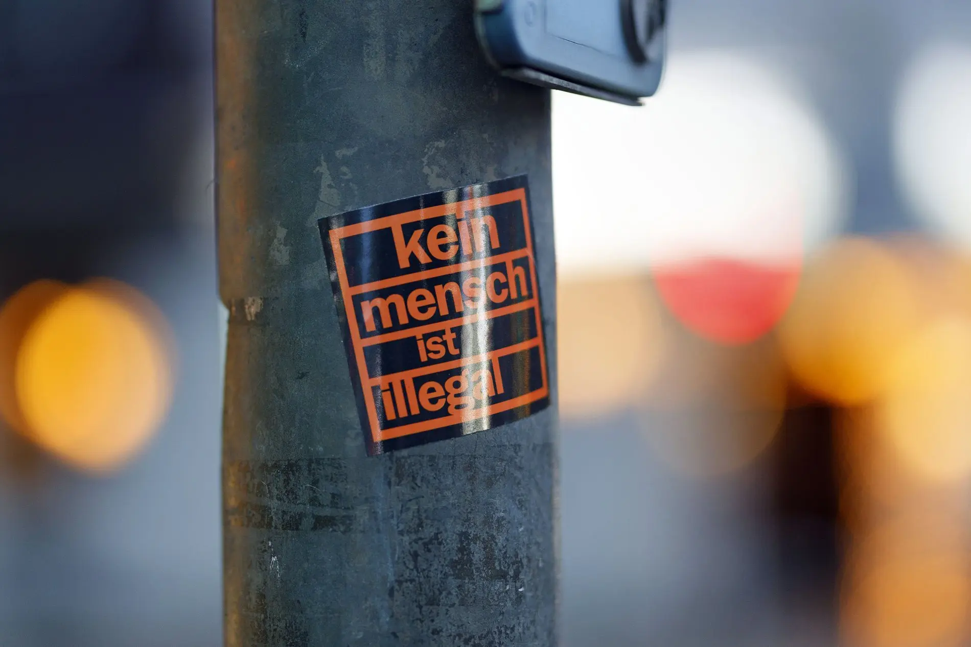 Ein Sticker mit der Aufschrift "Kein Mensch ist illegal" an einem Pfahl.