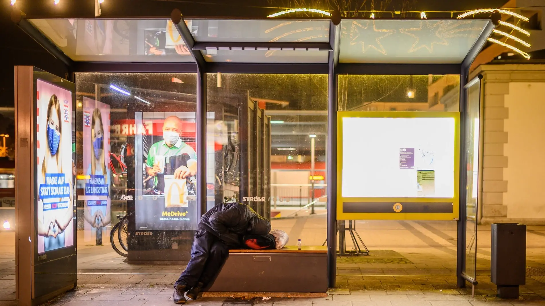 Ein Mensch übernachtet auf der Bank einer Berliner Bushaltestelle