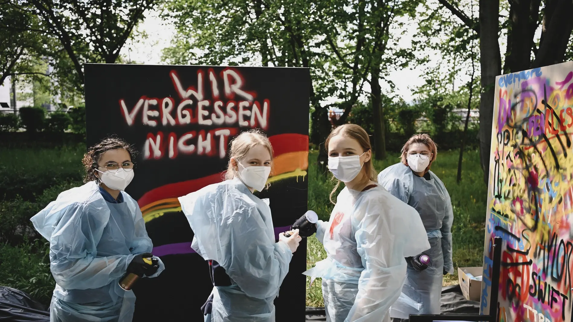 Graffiti-Workshop Mehrere Jugendliche mit Maleroutfits üben Graffiti an Wänden
