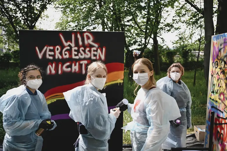 Mehrere Jugendliche mit Maleroutfits üben Graffiti an Wänden
