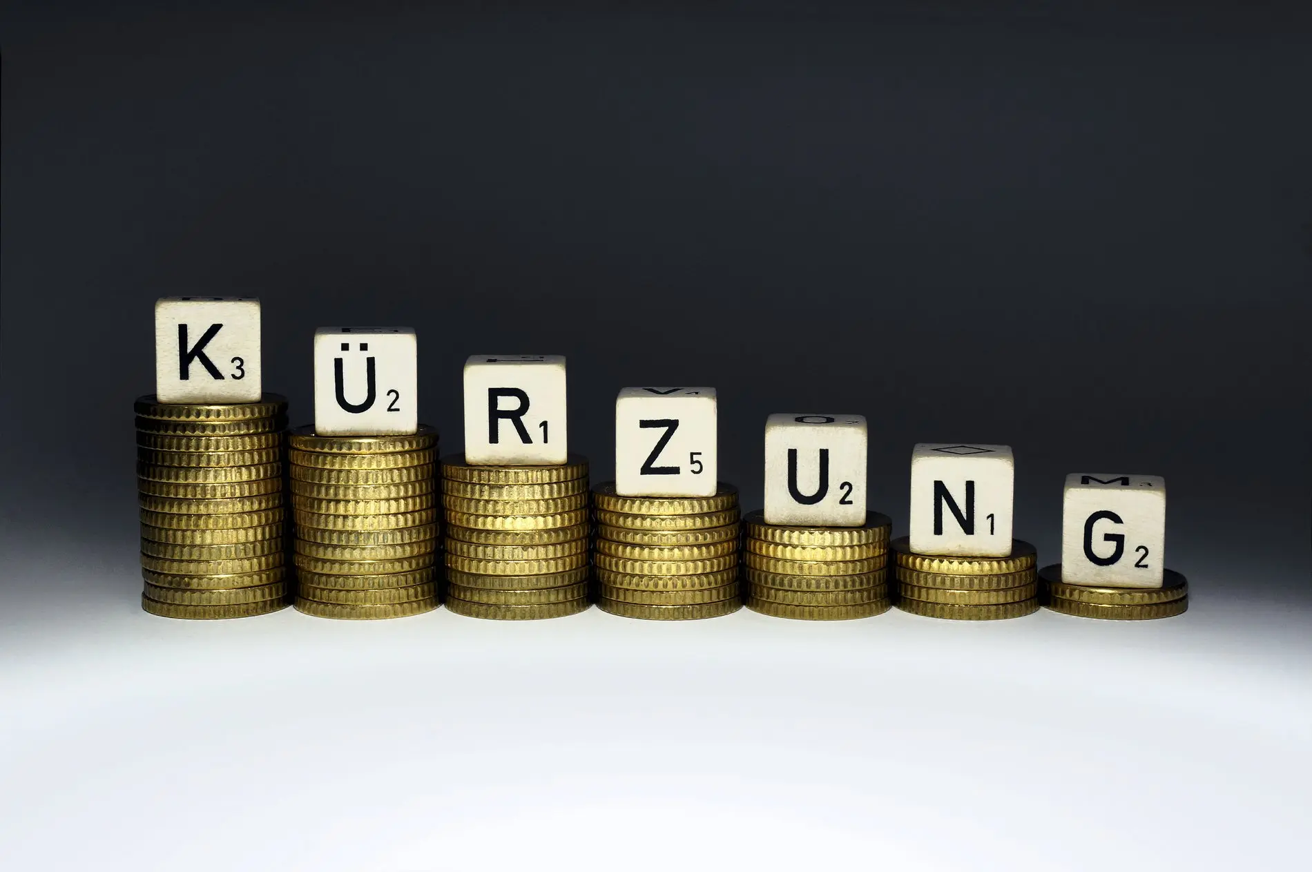 Buchstabenwürfel auf kleiner werdenden Geldstapeln bilden das Wort "Kürzung".