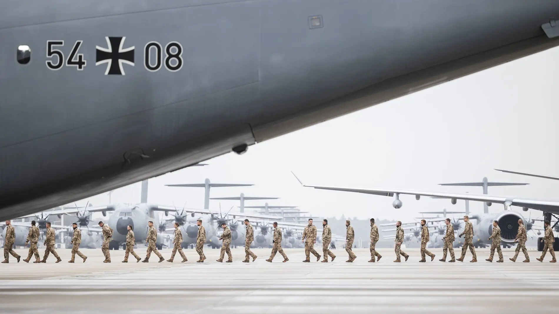 Soldatinnen und Soldaten der Bundeswehr laufen hintereinander, im Hintergrund Bundeswehrflugzeuge