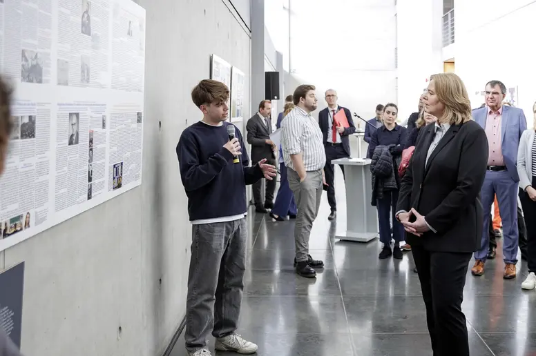 Ein Schüler stellt mit Mikrofon das siegreiche Projekt vor, Bärbel Bas hört zu