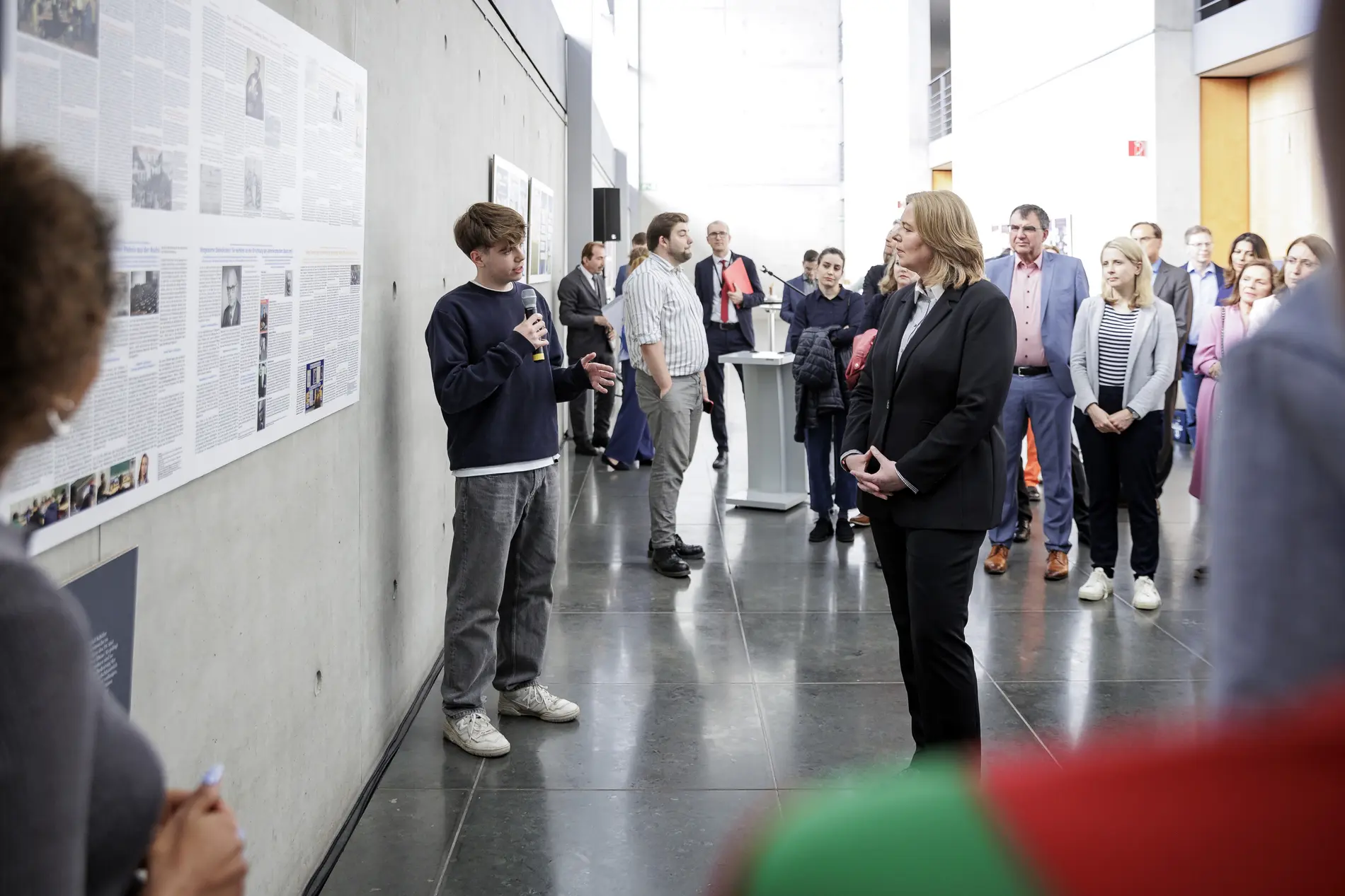 Ehrung der Gewinner beim Schülerwettbewerb Ein Schüler stellt mit Mikrofon das siegreiche Projekt vor, Bärbel Bas hört zu