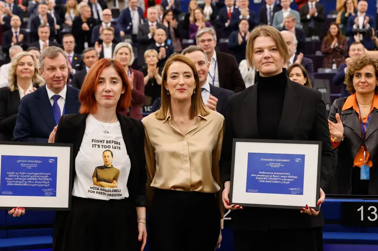 Die Präsidentin des Europäischen Parlaments steht zwischen zwei Personen zusammen, die eine Urkunde in den Händen halten.