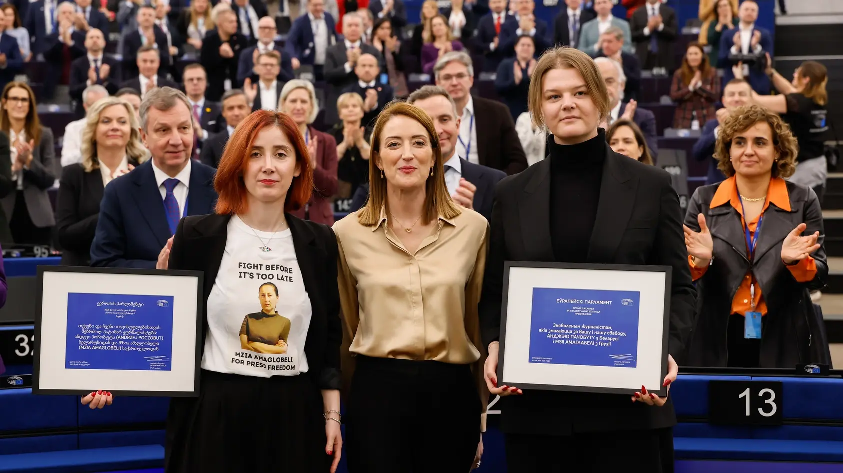 Die Präsidentin des Europäischen Parlaments steht zwischen zwei Personen zusammen, die eine Urkunde in den Händen halten.