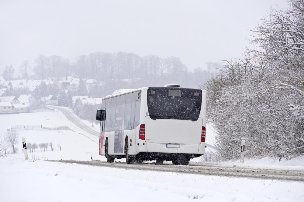 Regionalbus bei Schneegestöber und glatter Fahrbahn auf einer Landstraße.